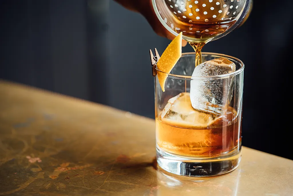 A close-up shot of a bartender pouring whiskey into a glass.