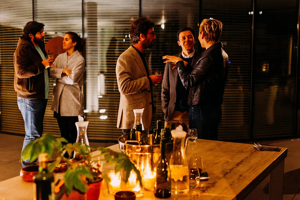 People chatting around a table at a corporate party with bottles of alcohol in a bucket in the foreground.