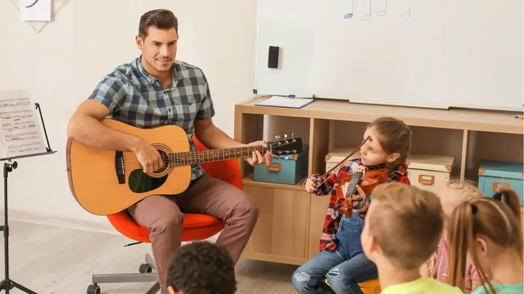 Music teacher in group setting holding a guitar.