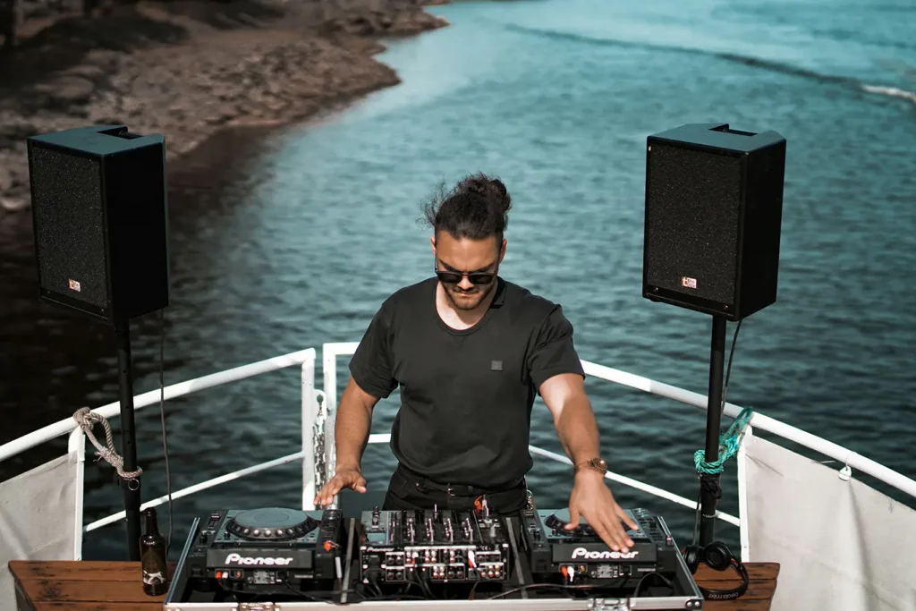 A DJ dressed in all black DJing on a boat.