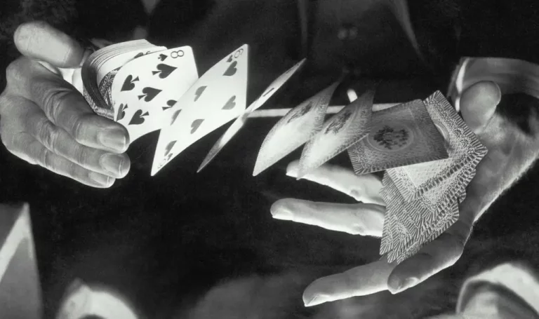 A black and white photo of a magicians hands doing a trick while shuffling a stack of playing cards in the air after buying magicians insurance.