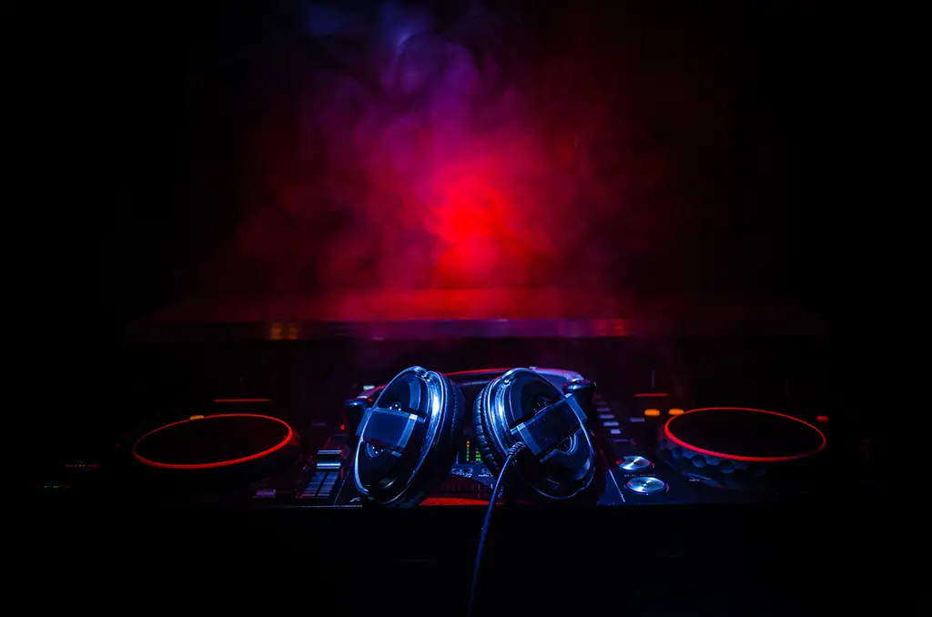 A pair of headphones resting on a turntable with a red light and fog in the background.