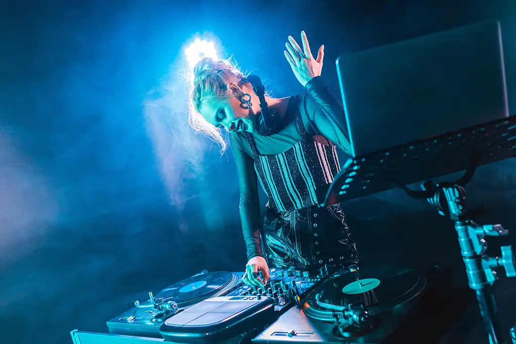 A DJ playing a set illuminated by a blue light and surrounded by fog.