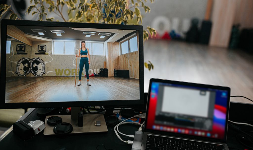 A laptop with a virtual personal training video is plugged into a desktop monitor so edited videos can be transferred for uploading and storing.