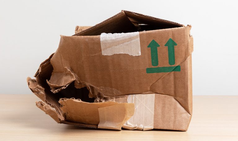 A broken cardboard box sits damaged and bent on the floor of a home.