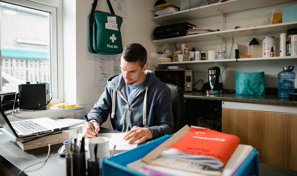 A personal trainer sits in his office where he works on paperwork for his business and getting personal trainer insurance.