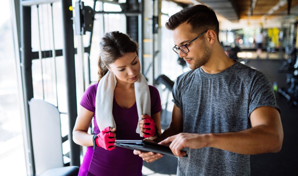 A personal trainer goes over his online hybrid plan for his client in the gym that she will follow on her own for the remainder of the week.