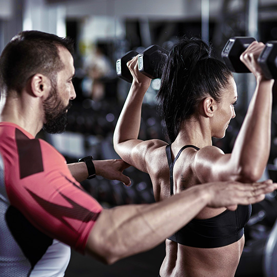 A personal Trainer spots a client and checks their form.