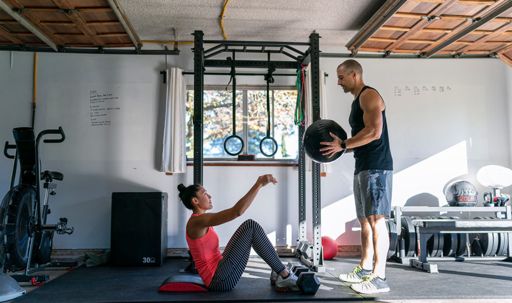 A freelance personal trainer is safely working with a client in her home gym knowing he is protected from dozens of risks with personal trainer insurance.