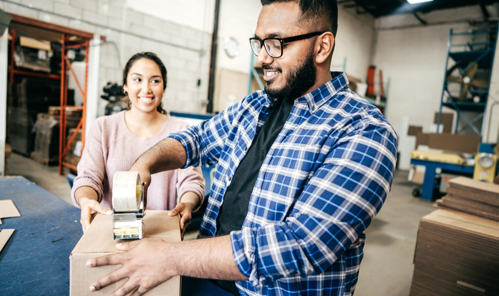 A man and a woman are chatting in a warehouse as they package up orders for their customers.