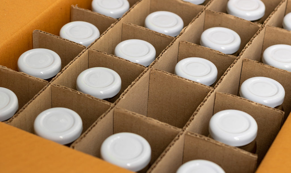The top view of a box has separators inside to keep glass bottles in place. One bottle is missing, but all the bottles are still insured with product liability insurance.