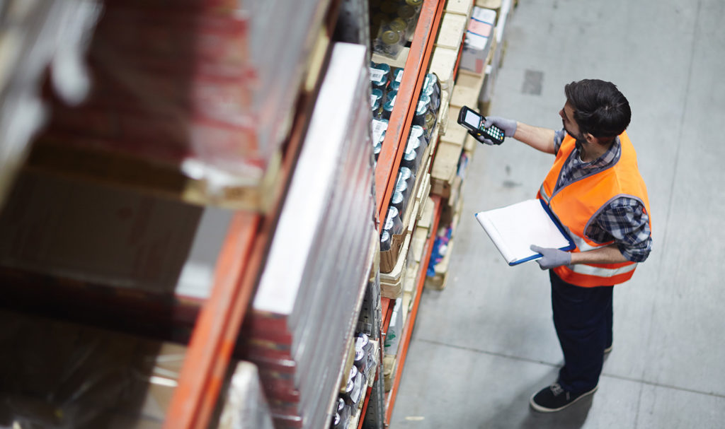 A warehouse worker in a reflective working vest is scanning the items in a warehouse to add them to his product liability insurance policy.