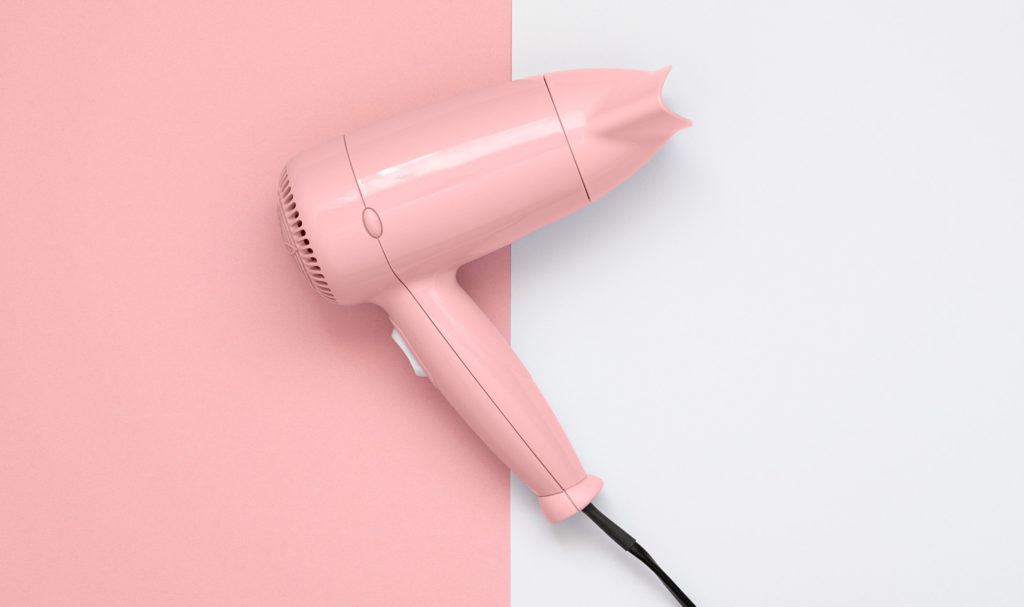A pink hair dryer is on a background that is split between pink and gray colors.