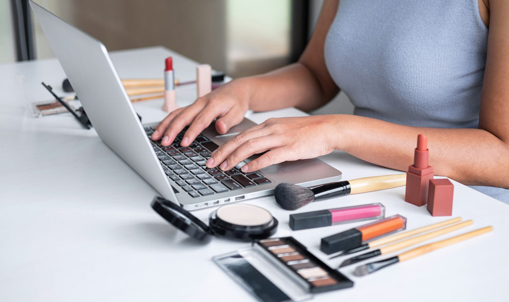 A woman works on her laptop on a desk surrounded by the different products she sells on her website.