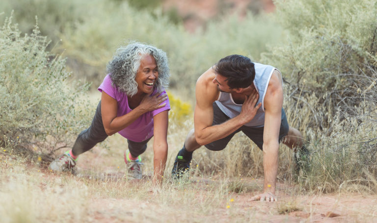 A personal trainer and his client are working out together outdoors amongst the plants.