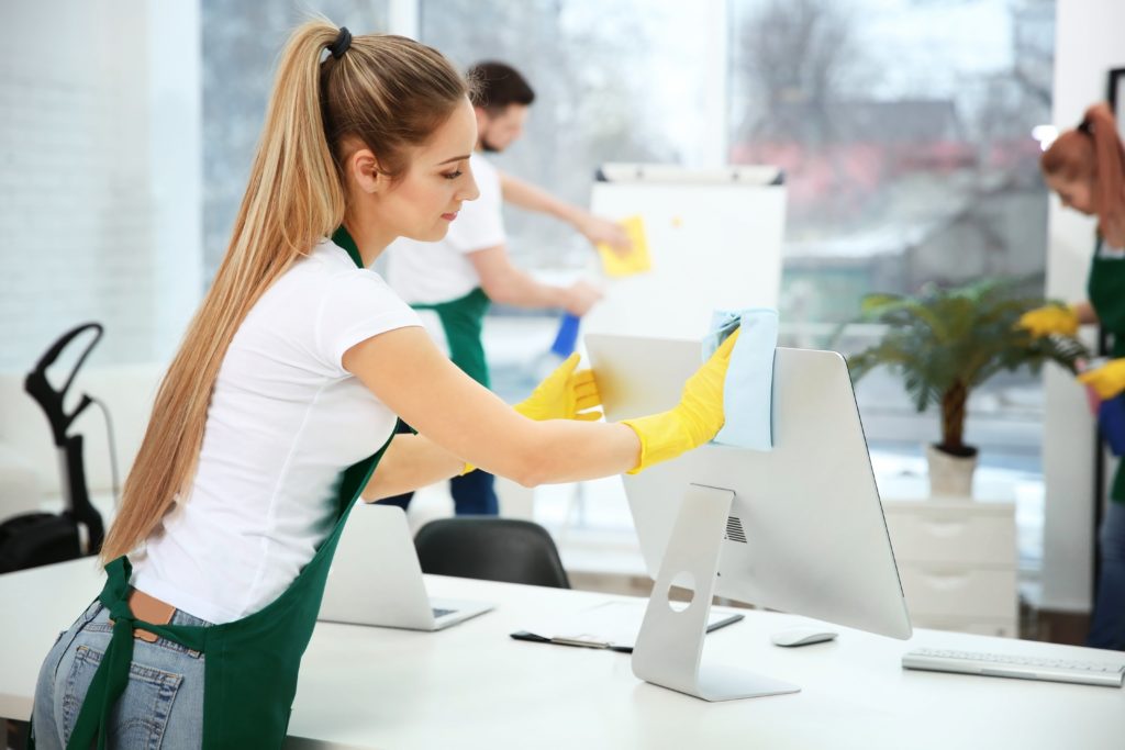 woman cleaning computer with group cleaning office