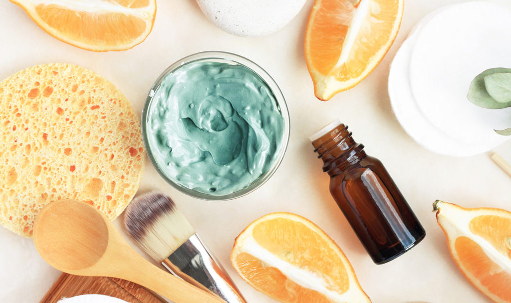 Citrus and creams are assorted on a white table with different tools to display the ingredients of a beauty product.
