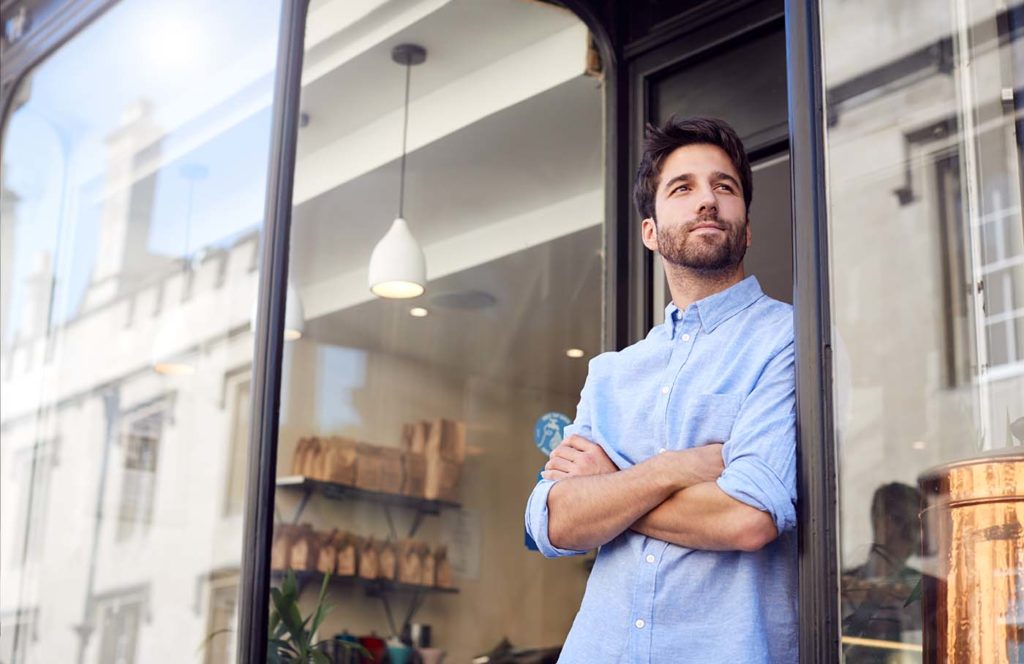 A retail store owner stands outside his shop doorway.