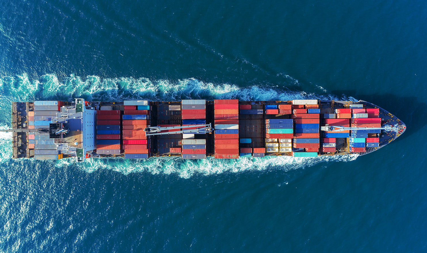 The overhead view of a cargo ship full of colorful shipping containers transporting products overseas with product liability insurance.