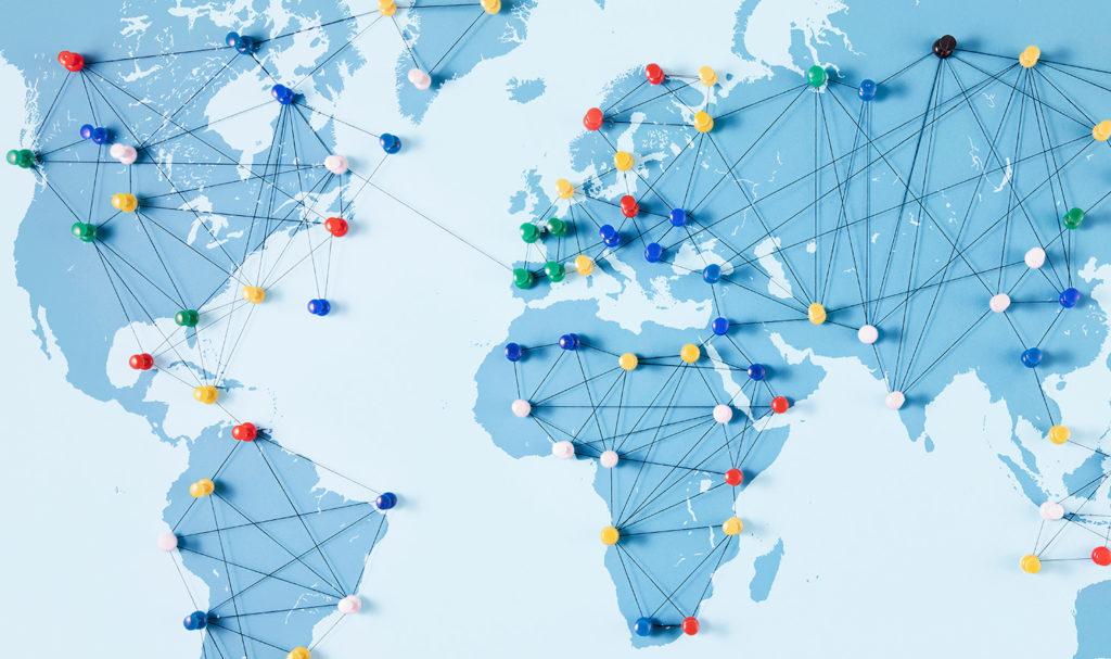 A blue map of the world with multi-colored thumbtacks and string connecting each tack are displaying a global business's main hubs around the world.