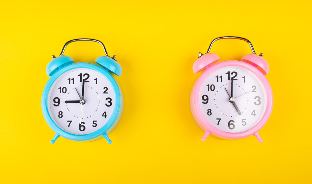 A blue and a pink clock on a yellow background