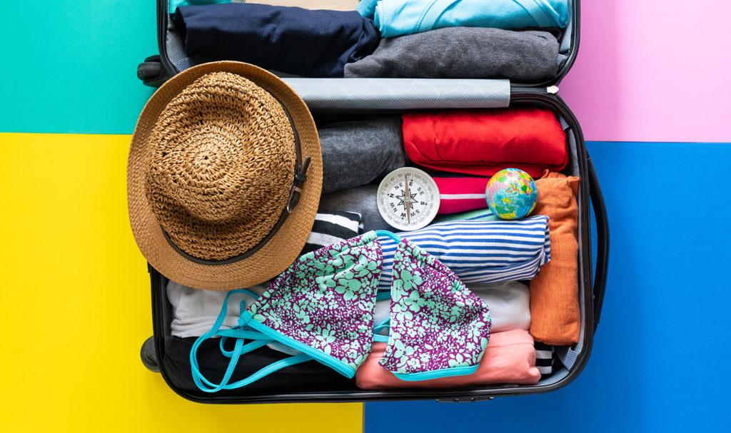A packed suitcase sits open on a pink, teal, yellow, and blue background.