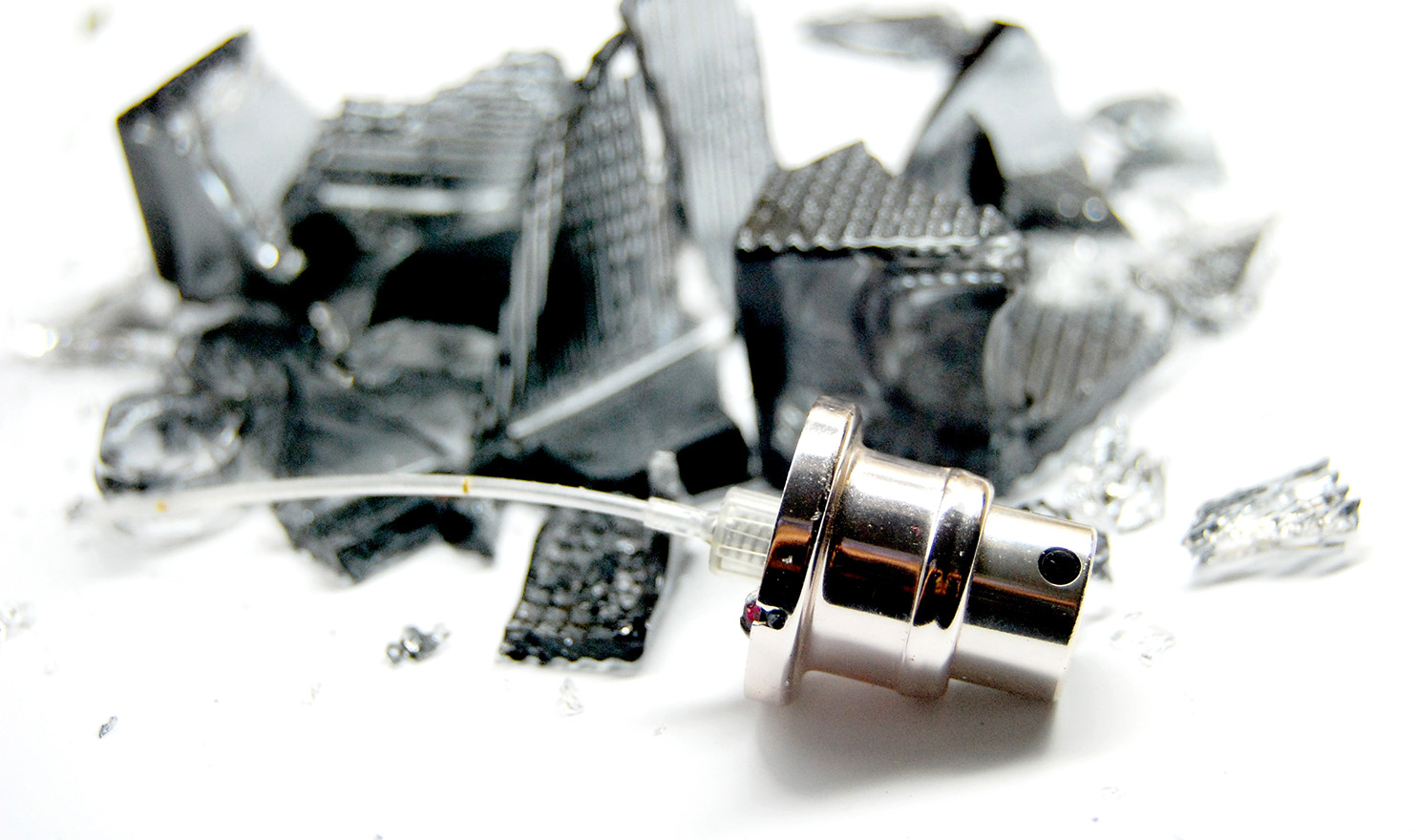 A broken black glass perfume bottle lays in pieces on a white background.