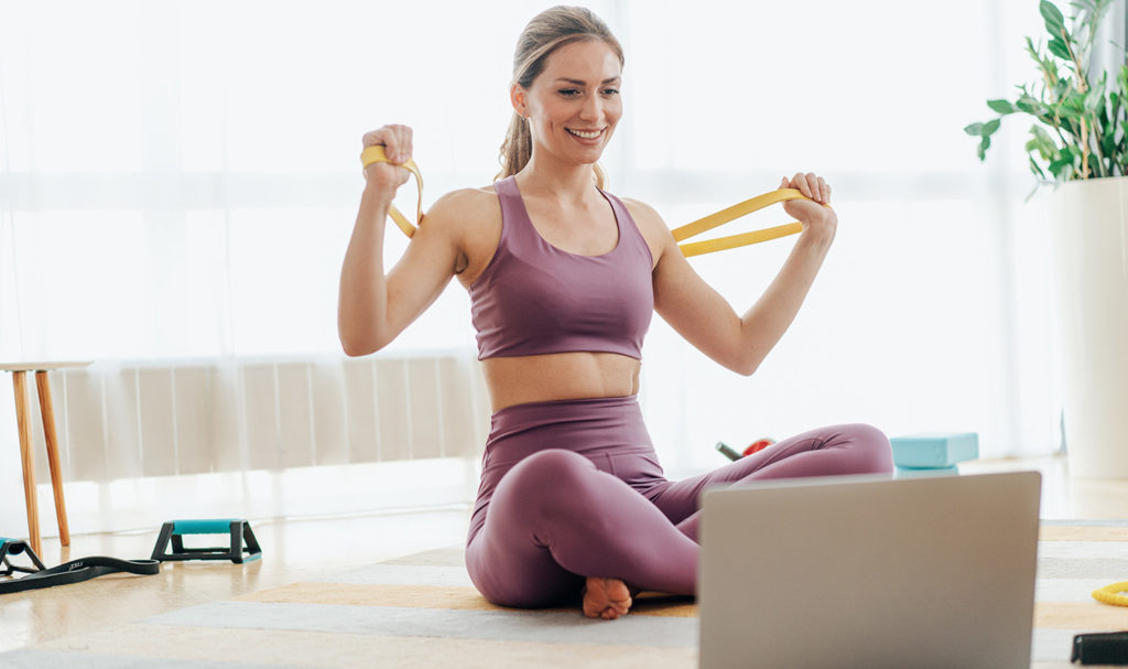 A yoga teacher smiles at her laptop as she completes her yoga teacher certification program and is getting ready to start teaching once she buys yoga teacher insurance.