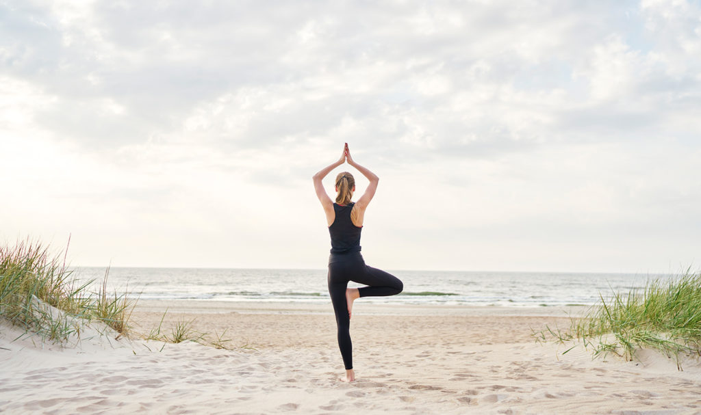 A yoga teacher poses on a beach after finishing certification and getting yoga teacher insurance.