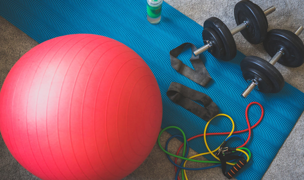 A red balance ball is resting on top of a blue yoga mat, along with weights, resistance bands, arm bands, and a water bottle. If the fitness equipment was faulty and broke, product liability insurance may help pay for the accidents caused.