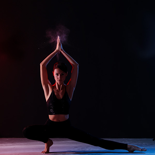 A yoga teacher works in a dramatically lit studio.