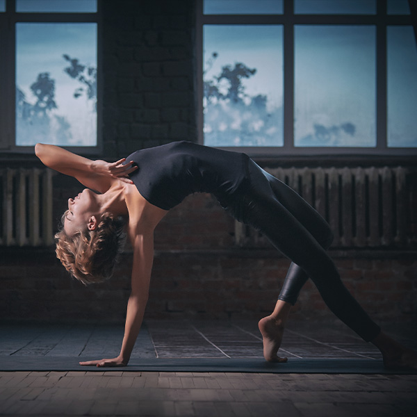 A yoga teacher practices yoga and bends backwards on one hand.