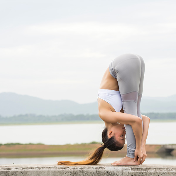 A yoga teacher practices yoga outside and folds her head towards her knees.