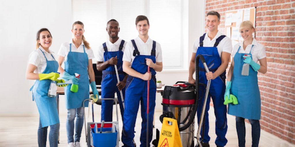 group of cleaners smiling together holding cleaning supplies and tools