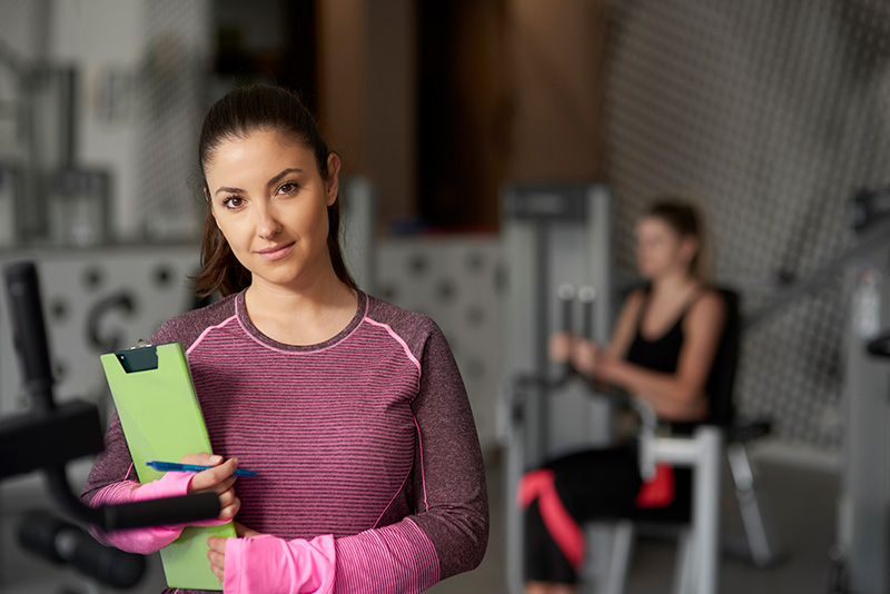 A personal trainer stands with a clipboard.