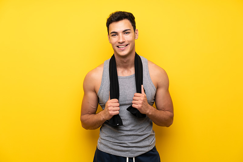 A personal trainer holds a towel and smiles in front of a yellow background.