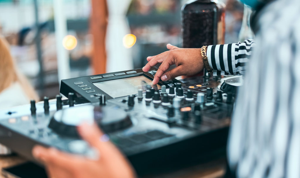 A close up shot of a DJ mixing music on his sound board at an event with general liability insurance.