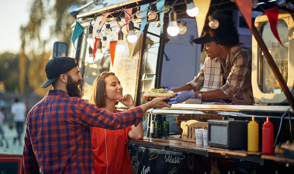 A food truck owner is handing over a meal to a customer.