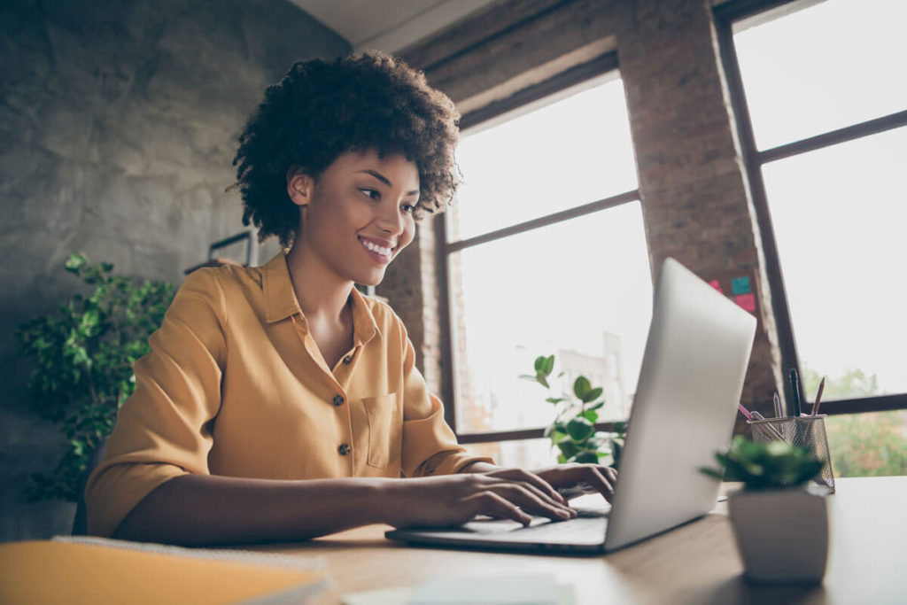 Person on laptop in office with brick walls and two windows.