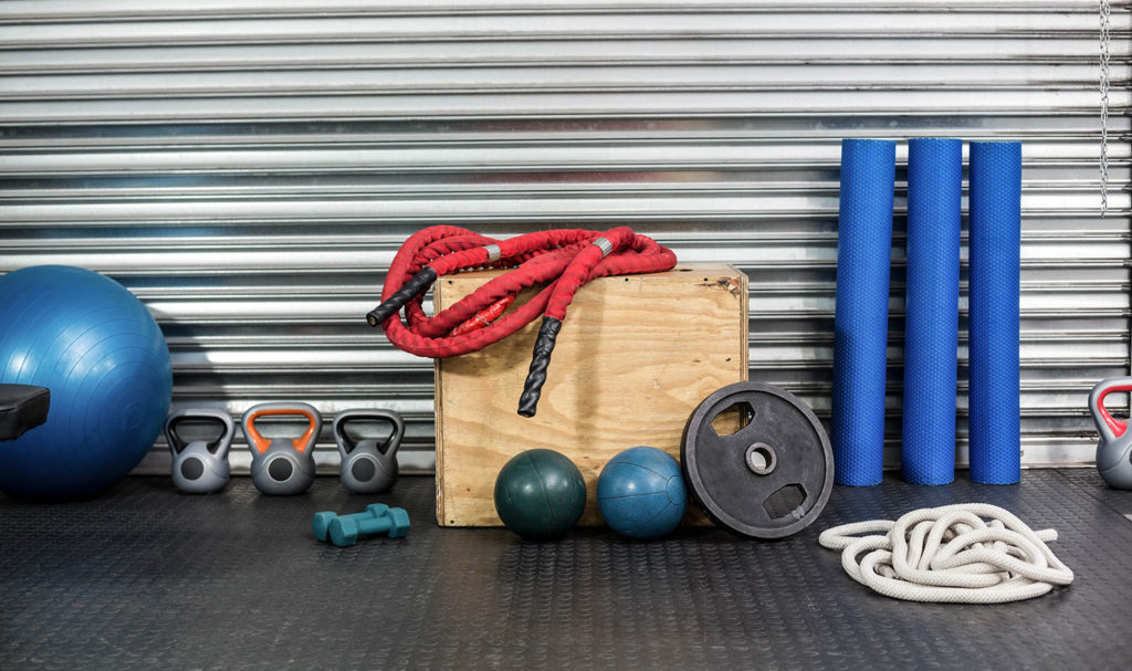 A pile of personal trainer equipment is lined up along a wall in a gym.