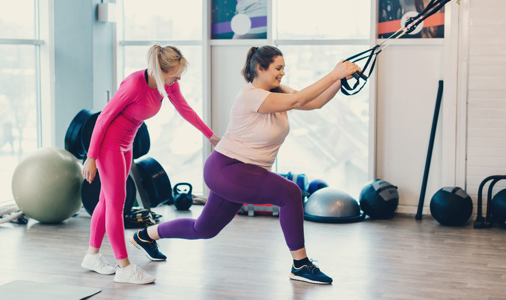 A trainer is helping her client learn how to workout with resistance bands in a private studio. The trainer was able to start her own business after establishing a good fitness business names.