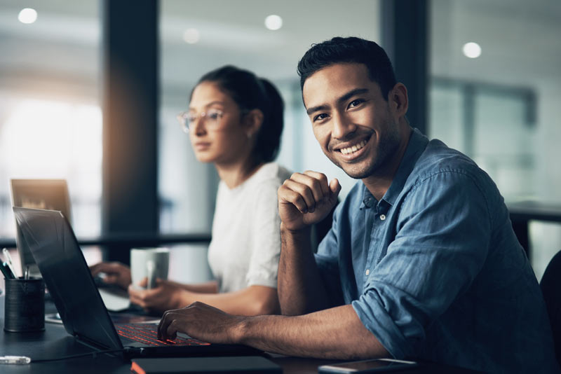 Man smiling at the camera while working on a laptop