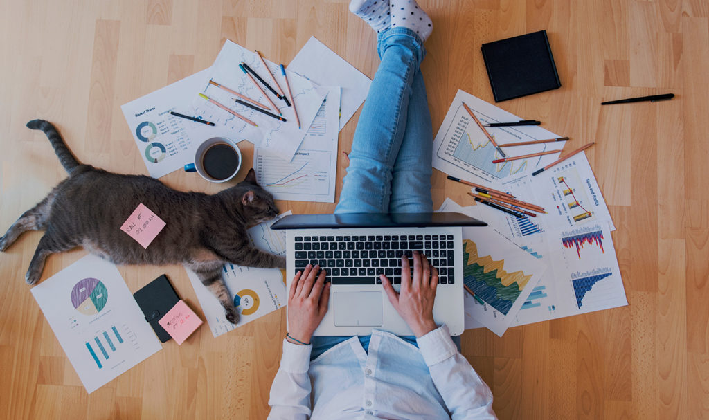 A person is sitting on the ground amongst paperwork for their business as they work on their laptop to apply for a product insurance quote.