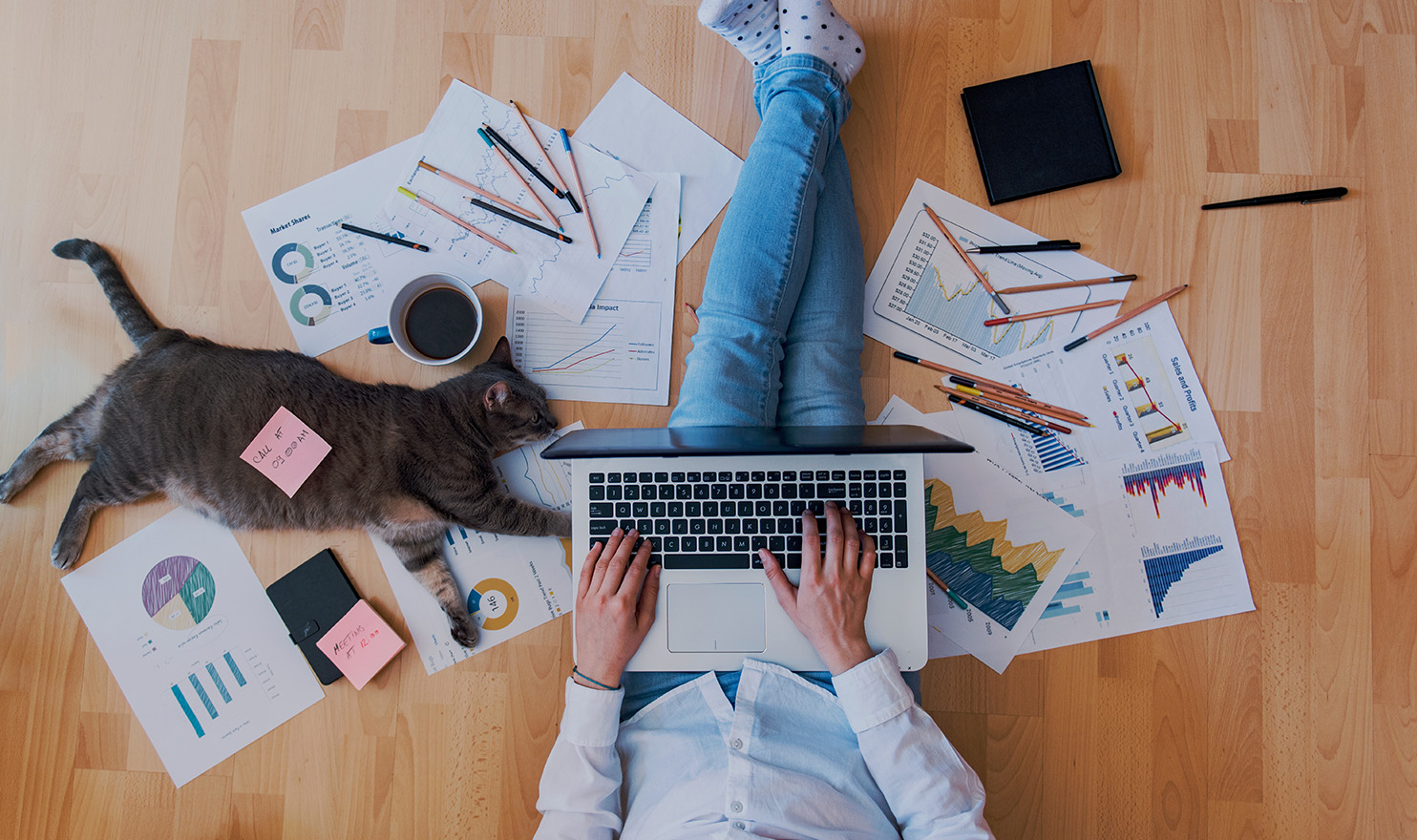 A person is sitting on the ground amongst paperwork for their business as they work on their laptop to apply for a product insurance quote.