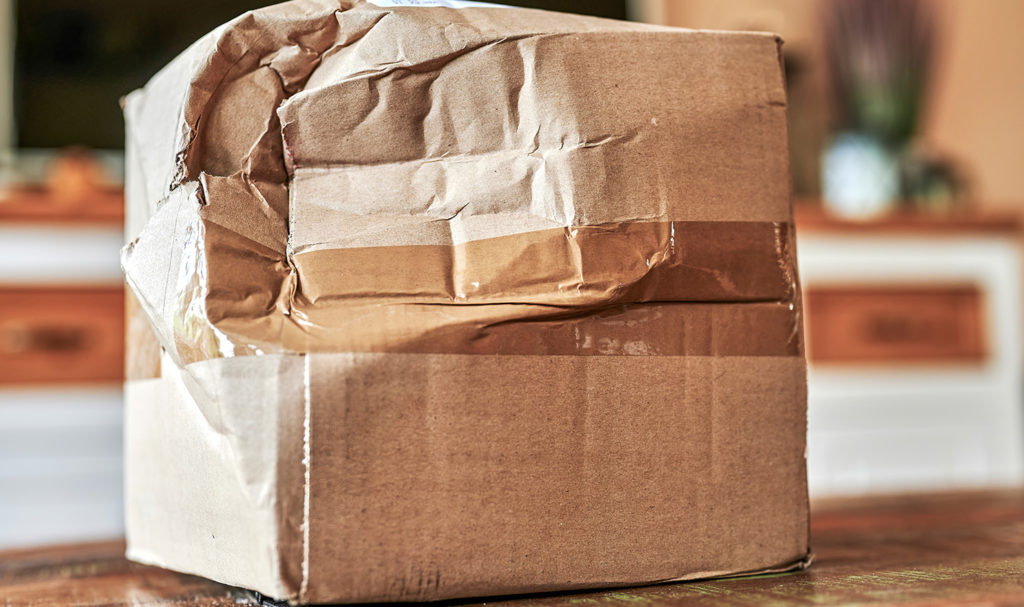 A damaged cardboard box is sitting on a desk in a home office.