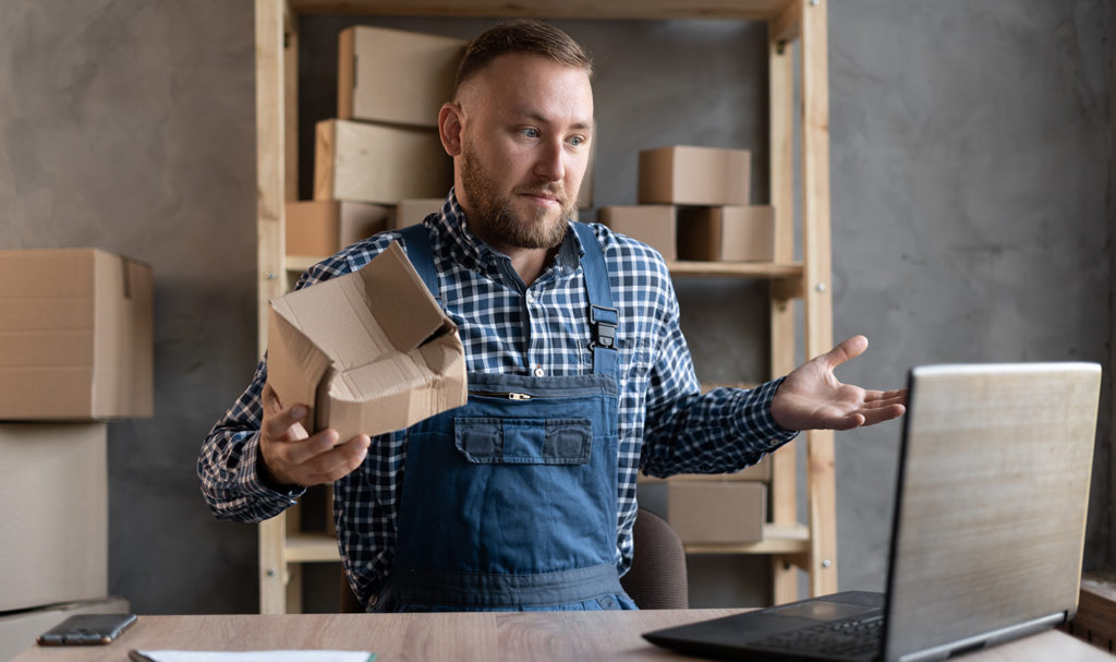 A man with a broken product shrugs toward his computer as he looks to get a product liability insurance quote.