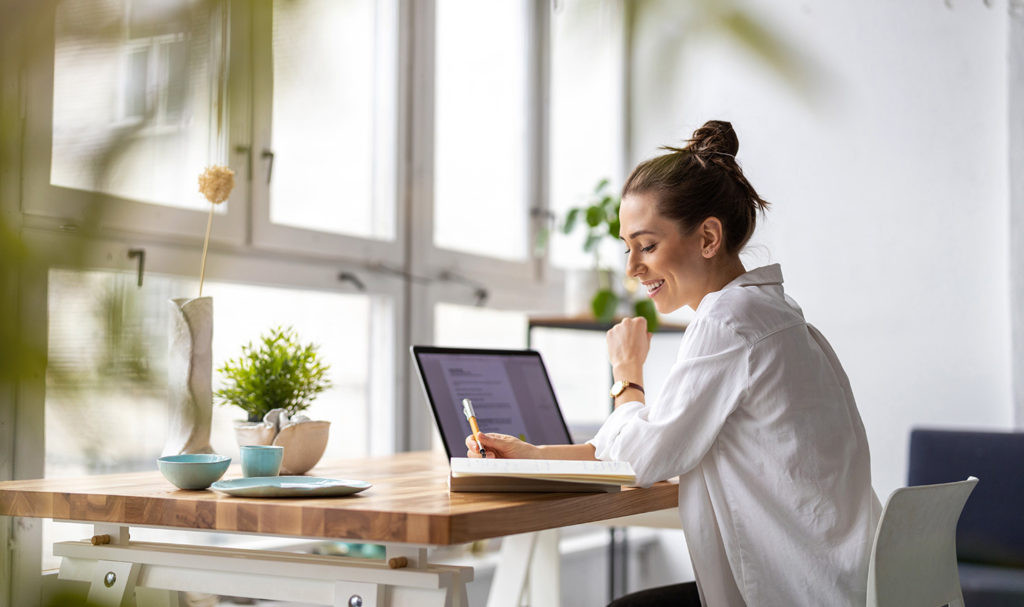 A woman takes notes while they work in their home and apply for a product liability quote online.