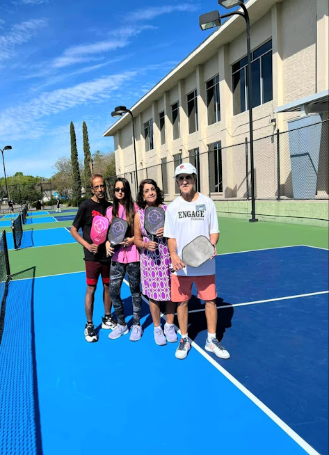 Ram posing for a photo with some students on an outdoor pickleball court.