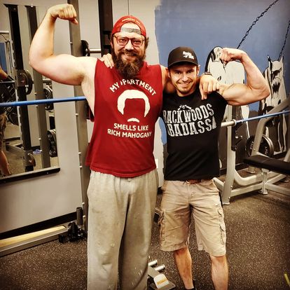 Josh posing with a client as they flex their biceps to show off the muscles they have worked hard for.