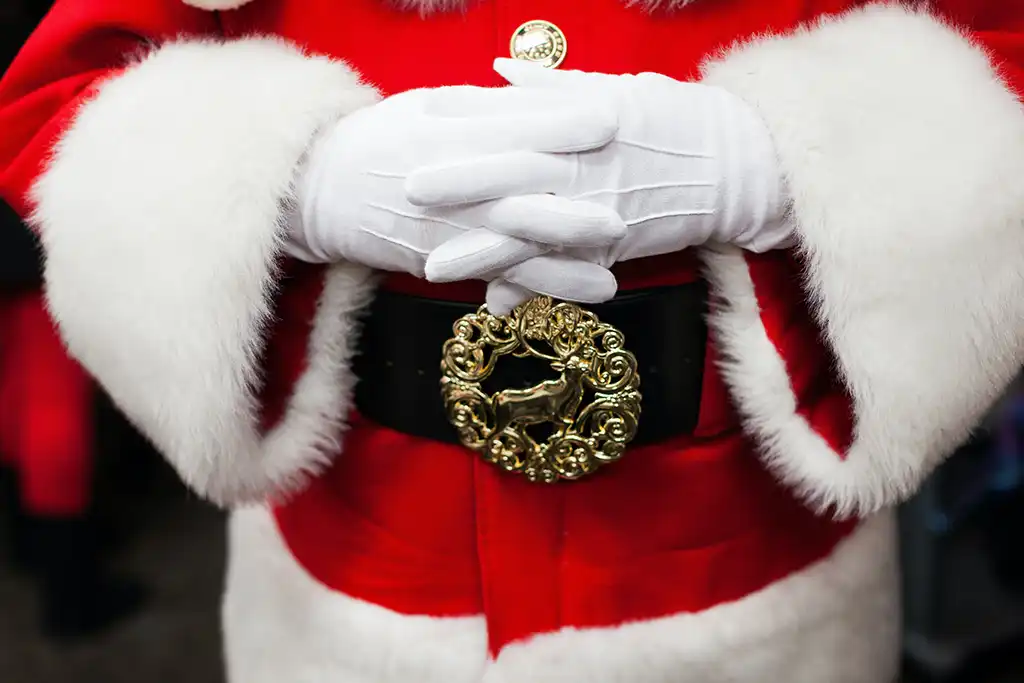 A close-up shot of a Santa holding his hands above a gold belt buckle with a reindeer design.